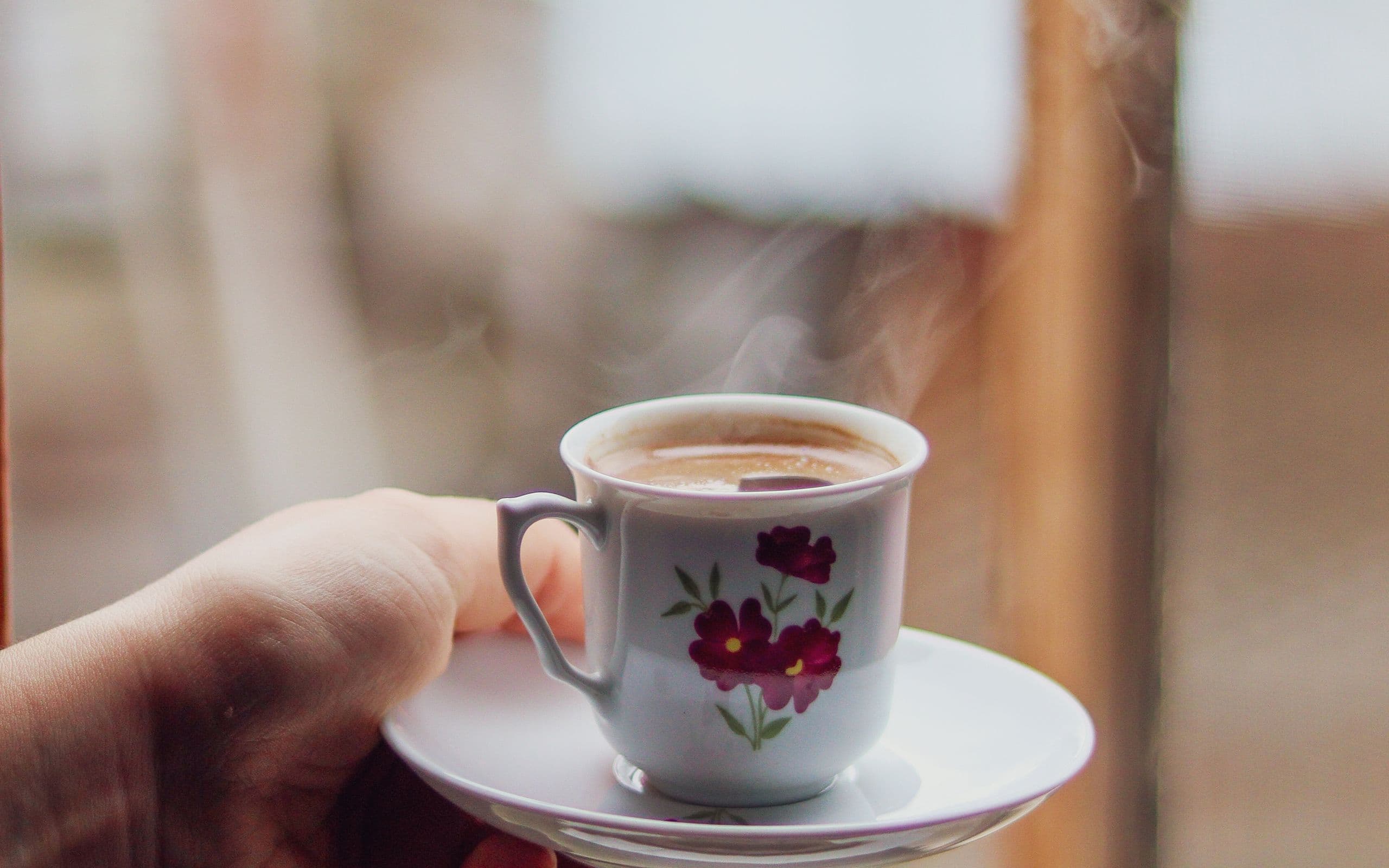Une main tient une tasse chaude près d'une fenêtre, un moment de pause.