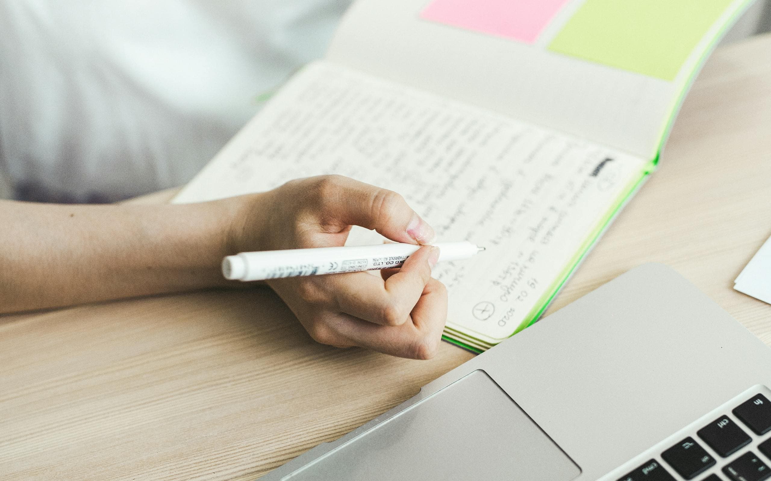 Une main prend des notes dans un carnet, à côté d'un ordinateur portable.